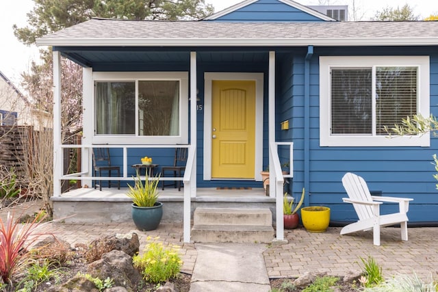 entrance to property with covered porch, a shingled roof, and fence