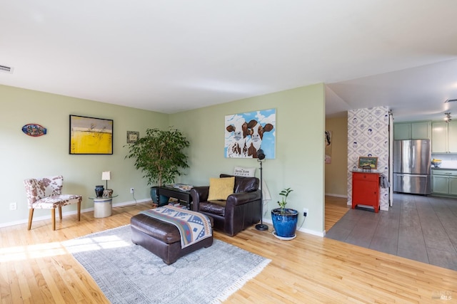 living area with baseboards, visible vents, and wood finished floors