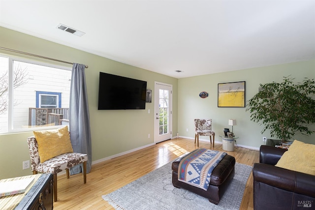 living area featuring baseboards, visible vents, and light wood finished floors