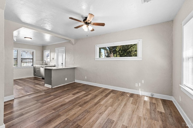 unfurnished living room with a ceiling fan, baseboards, dark wood finished floors, and a sink
