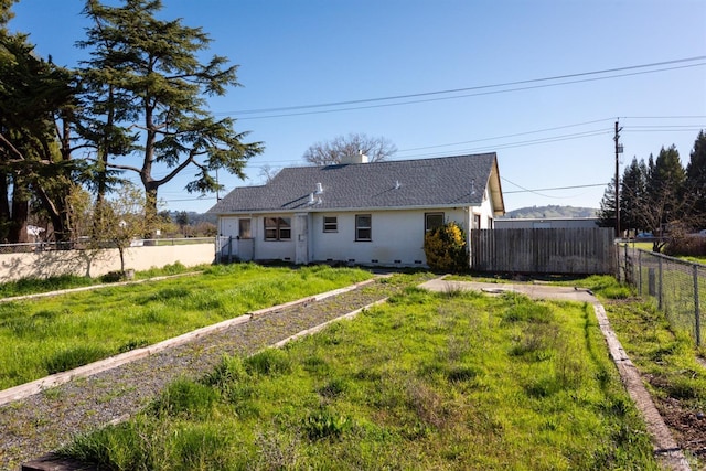 back of house with a shingled roof, a lawn, a fenced backyard, crawl space, and stucco siding