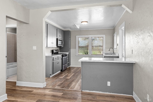kitchen featuring gray cabinetry, stainless steel appliances, dark wood finished floors, and a textured wall