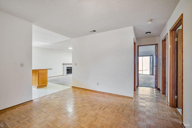 empty room featuring baseboards, a fireplace, visible vents, and a textured ceiling