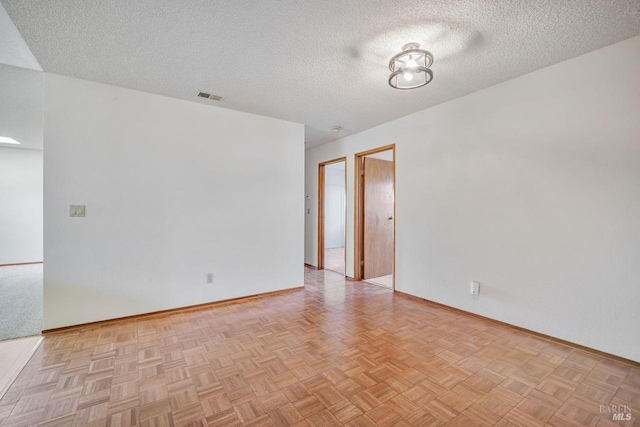 spare room featuring a textured ceiling, visible vents, and baseboards