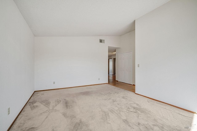 unfurnished room featuring baseboards, visible vents, vaulted ceiling, a textured ceiling, and carpet floors