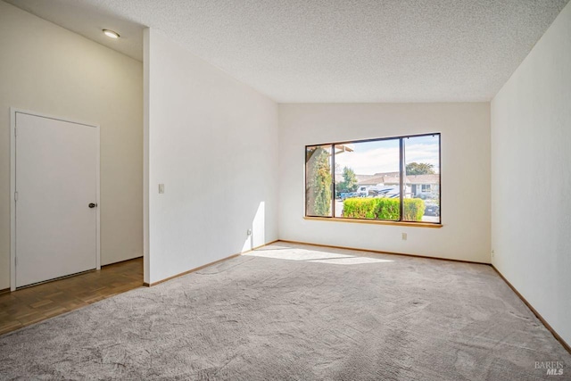 carpeted spare room with lofted ceiling, a textured ceiling, and baseboards