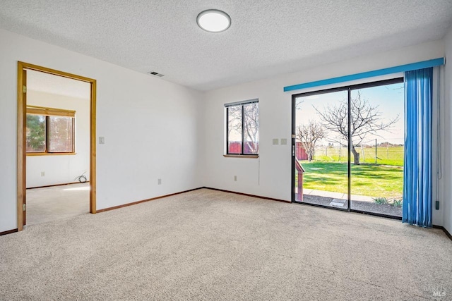 spare room featuring carpet floors, visible vents, a textured ceiling, and baseboards