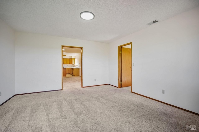 spare room featuring baseboards, a textured ceiling, visible vents, and carpet flooring