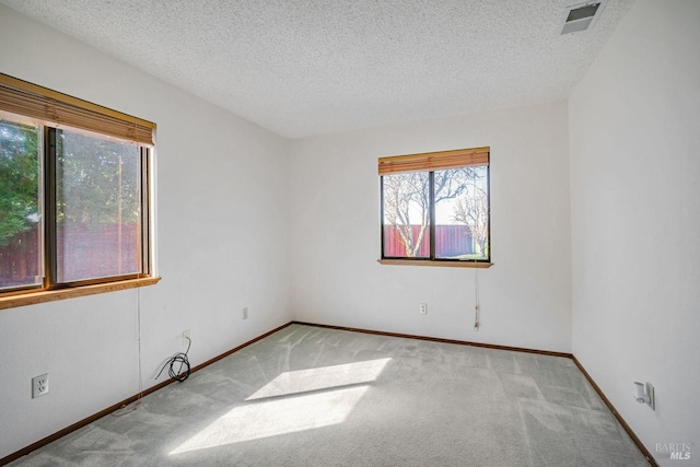 carpeted spare room with baseboards, visible vents, and a textured ceiling