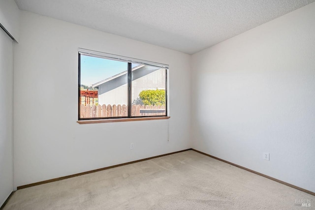 unfurnished room with light carpet, a textured ceiling, and baseboards