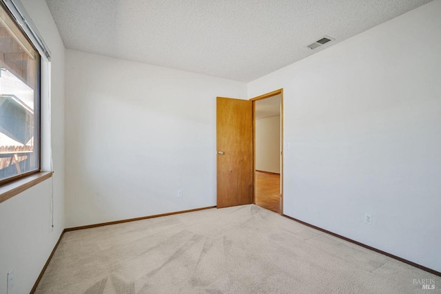 empty room with carpet floors, baseboards, visible vents, and a textured ceiling