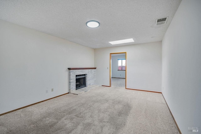 unfurnished living room with carpet floors, a skylight, visible vents, baseboards, and a brick fireplace