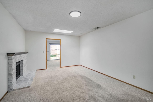 unfurnished living room with a fireplace, a skylight, visible vents, carpet flooring, and baseboards