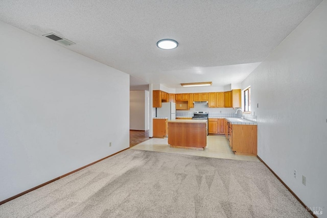 kitchen with visible vents, a center island, freestanding refrigerator, light countertops, and under cabinet range hood