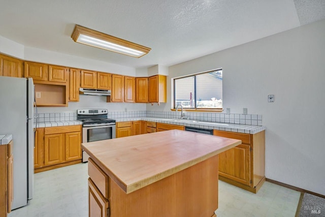 kitchen with under cabinet range hood, electric stove, freestanding refrigerator, a center island, and light floors