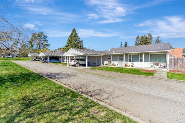 ranch-style home with an attached carport, gravel driveway, fence, and a front lawn