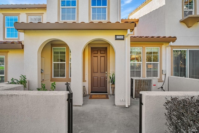 view of exterior entry featuring cooling unit, a tile roof, and stucco siding