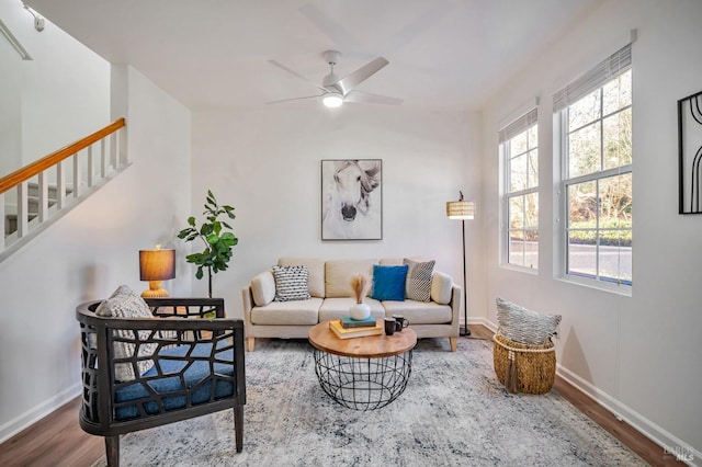 living area with ceiling fan, stairway, baseboards, and wood finished floors