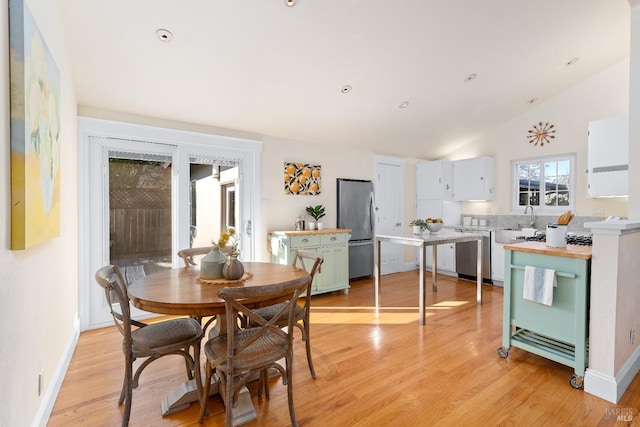 dining space featuring light wood-type flooring, lofted ceiling, and baseboards