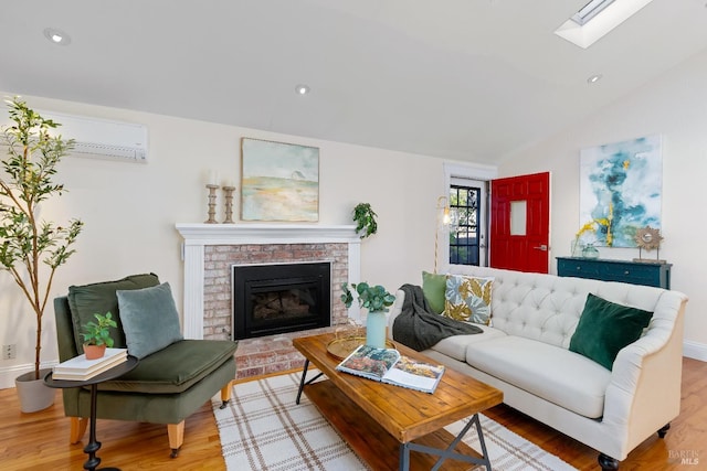 living area with vaulted ceiling with skylight, wood finished floors, a wall mounted air conditioner, a fireplace, and recessed lighting