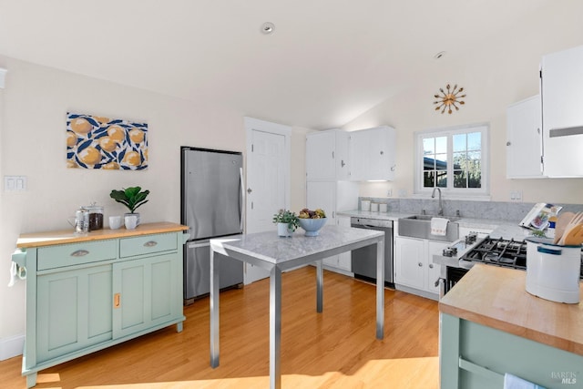 kitchen with stainless steel appliances, lofted ceiling, white cabinets, a sink, and light wood-type flooring