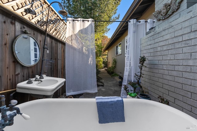 bathroom with a soaking tub, brick wall, and a sink