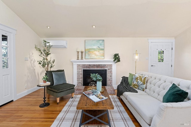 living room featuring lofted ceiling, wood finished floors, baseboards, a wall mounted AC, and a brick fireplace