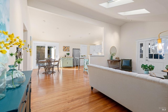 living area featuring light wood-style floors, a skylight, and high vaulted ceiling