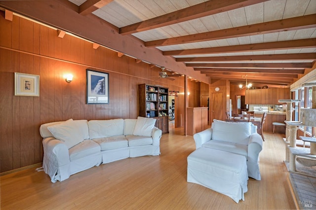 living room with vaulted ceiling with beams, ceiling fan with notable chandelier, light wood-type flooring, and wooden walls