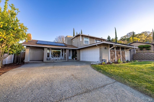 view of front facade featuring aphalt driveway, roof mounted solar panels, fence, a garage, and a front lawn