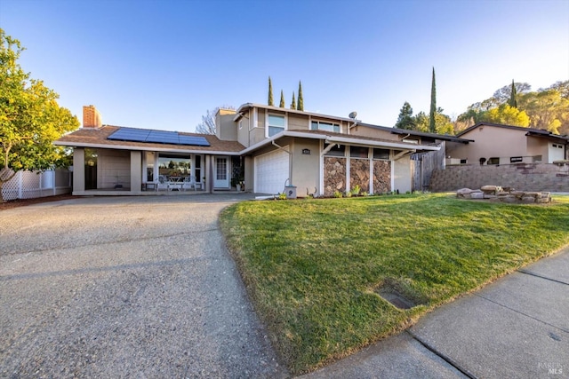 view of front of house featuring aphalt driveway, solar panels, an attached garage, fence, and a front lawn