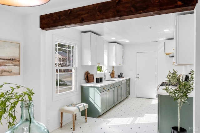 kitchen with light floors, light countertops, white cabinetry, a sink, and baseboards