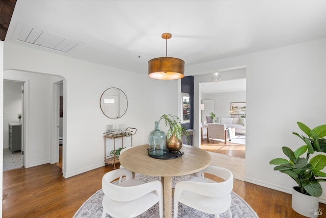 dining area with arched walkways, wood finished floors, and baseboards