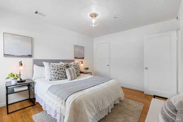 bedroom with wood finished floors, visible vents, and baseboards