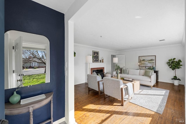 living room featuring a brick fireplace, crown molding, visible vents, and wood finished floors