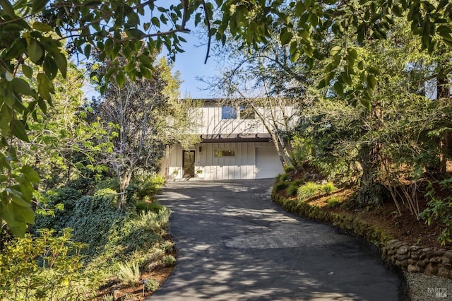 view of property hidden behind natural elements with board and batten siding, driveway, and an attached garage