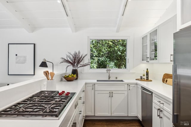 kitchen featuring beam ceiling, stainless steel appliances, light countertops, glass insert cabinets, and a sink