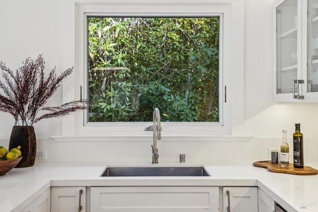 kitchen with light countertops, a sink, glass insert cabinets, and white cabinets