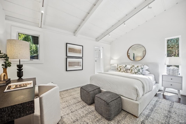 bedroom with baseboards, lofted ceiling with beams, ensuite bath, wood finished floors, and track lighting