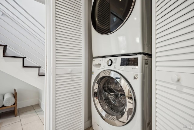 clothes washing area featuring laundry area, light tile patterned floors, baseboards, and stacked washer and clothes dryer