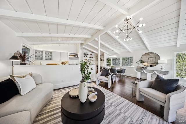 living room with lofted ceiling with beams, a notable chandelier, wood finished floors, and a healthy amount of sunlight