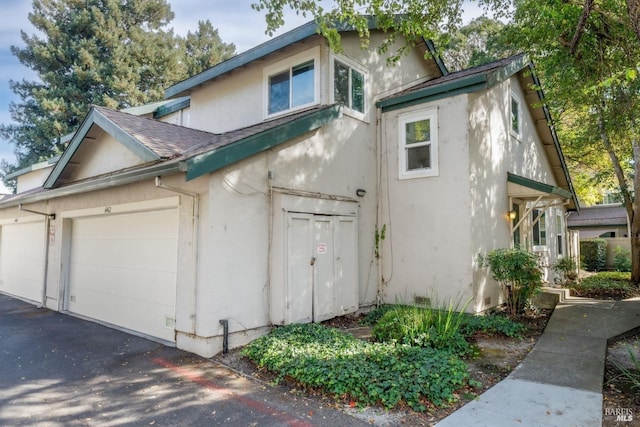 view of home's exterior with roof with shingles, an attached garage, and stucco siding