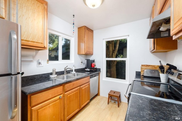 kitchen with light wood-style flooring, dark stone countertops, stainless steel appliances, under cabinet range hood, and a sink