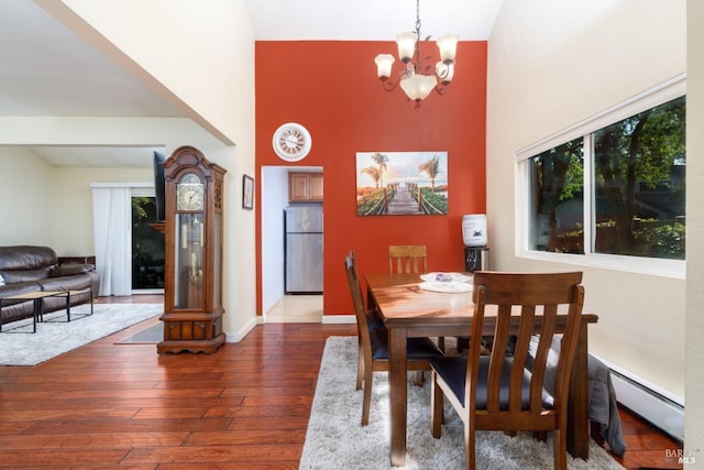 dining room featuring a towering ceiling, a notable chandelier, baseboards, and hardwood / wood-style floors