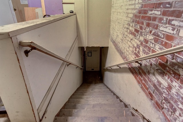 stairs with brick wall, wood finished floors, and electric panel