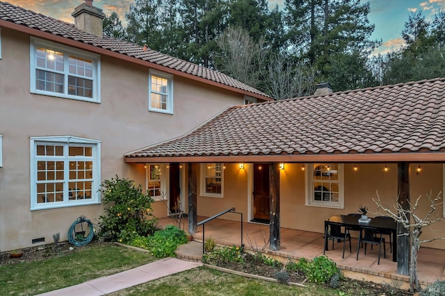 back of house with stucco siding, a tile roof, a chimney, and a patio