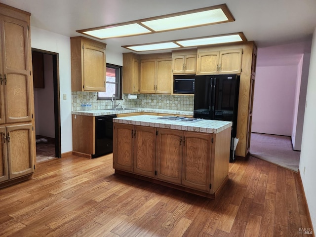 kitchen with light wood-style flooring, a kitchen island, a sink, backsplash, and black appliances