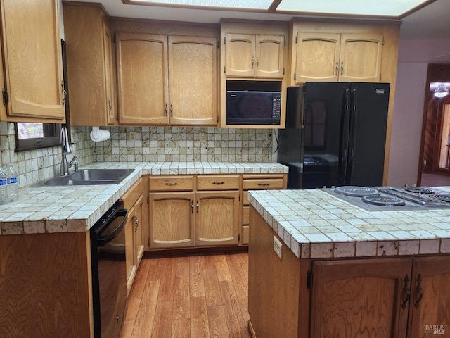 kitchen with black appliances, tasteful backsplash, light wood finished floors, and a sink