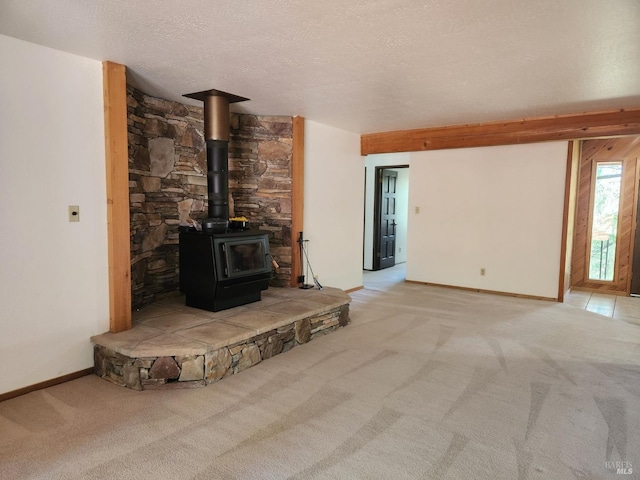 unfurnished living room featuring baseboards, a textured ceiling, a wood stove, and light colored carpet