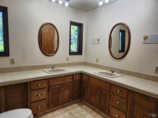 full bathroom with double vanity, a sink, and wallpapered walls